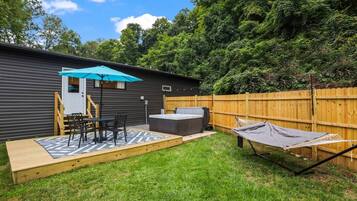 Ein Garten mit Whirlpool, Hängematte und einer Terrasse, komplett mit Tisch und Stühlen.