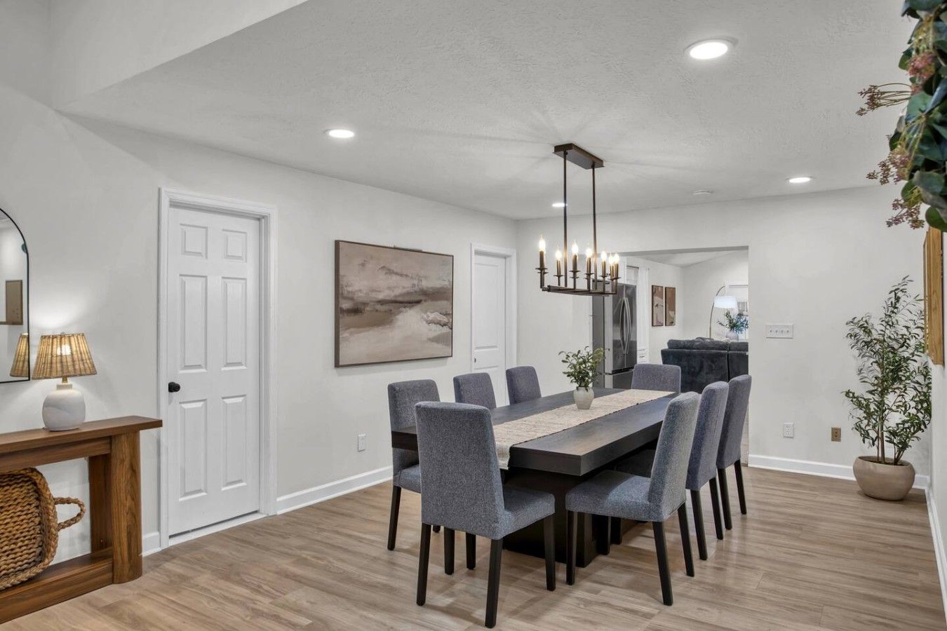 Un espace repas moderne avec une table rectangulaire, des chaises à revêtement gris, un luminaire suspendu et un grand tableau abstrait accroché au mur.