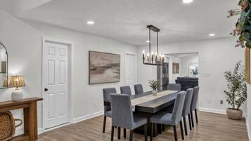 A modern dining area with a rectangular table, grey upholstered chairs, a hanging light fixture, and a large abstract painting on the wall.