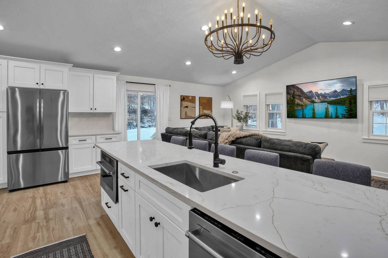 A modern kitchen with a large island, stainless steel appliances, and a chandelier.