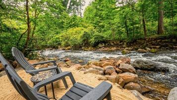 A riverside seating area with chairs and a table, surrounded by rocks and dense greenery.