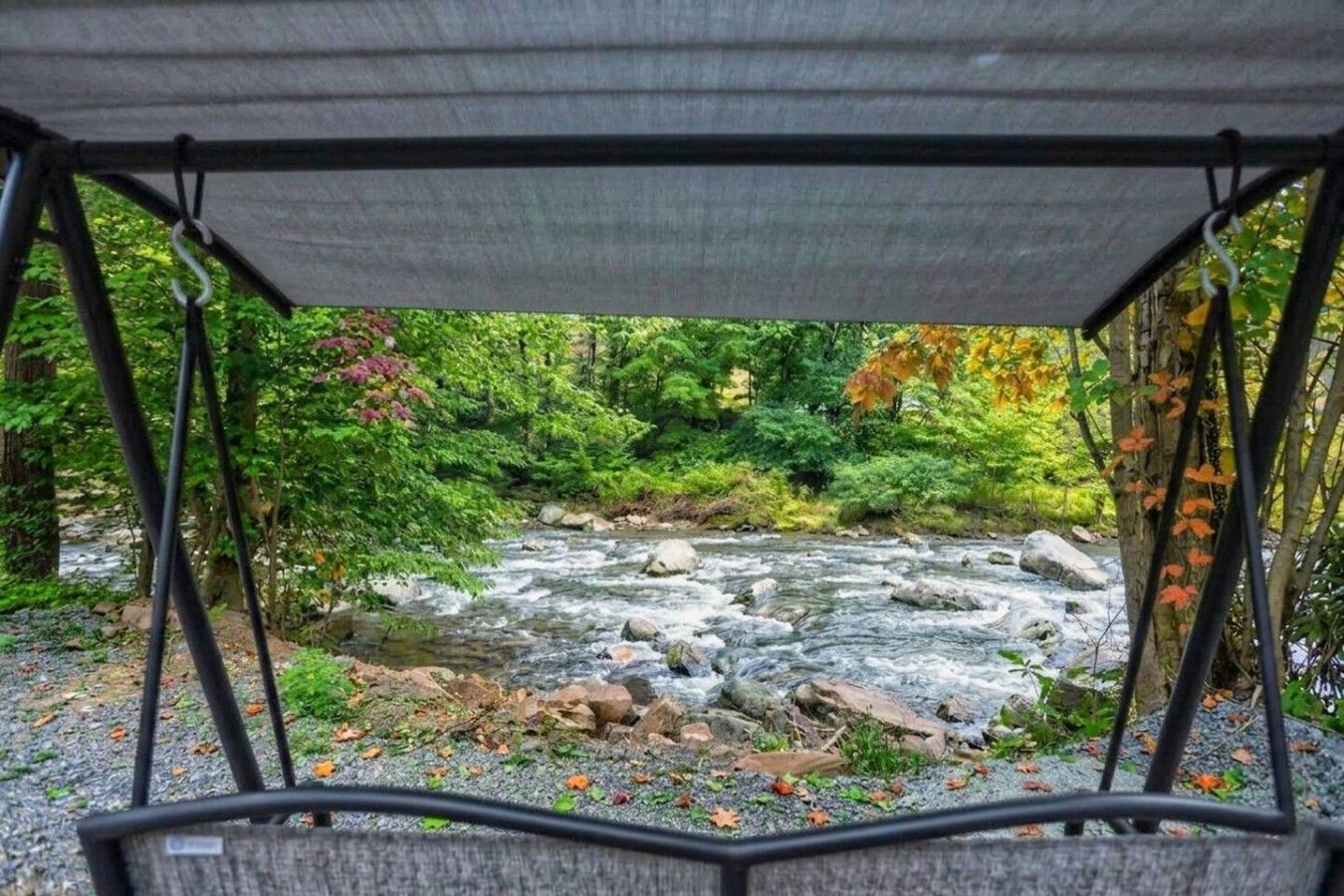 A covered seating area overlooking a flowing river with surrounding greenery.