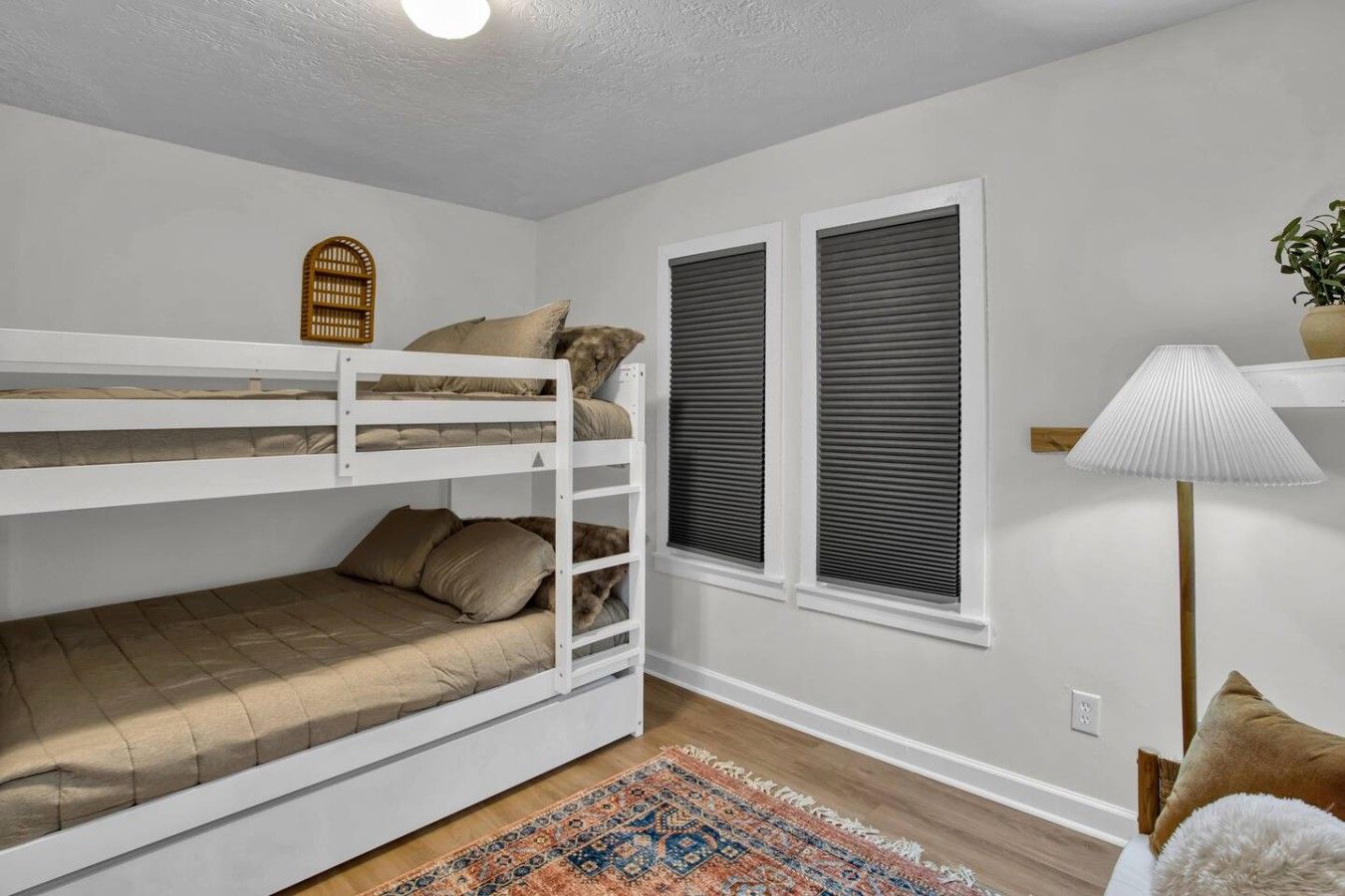 Een slaapkamer met een stapelbed, een kamerbreed tapijt met patroon, een lamp en een raam met jaloezieën.