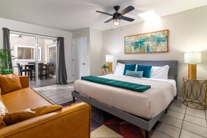 Una habitación de hotel con cama, sofá, zona de comedor y ventilador de techo.