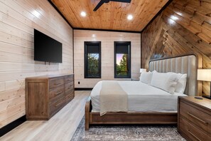 Un dormitorio con cama, televisor, cómoda y dos ventanas.