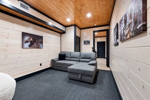 Ein Zimmer mit einem grauen Ecksofa, Holzvertäfelung und Kunstwerken.