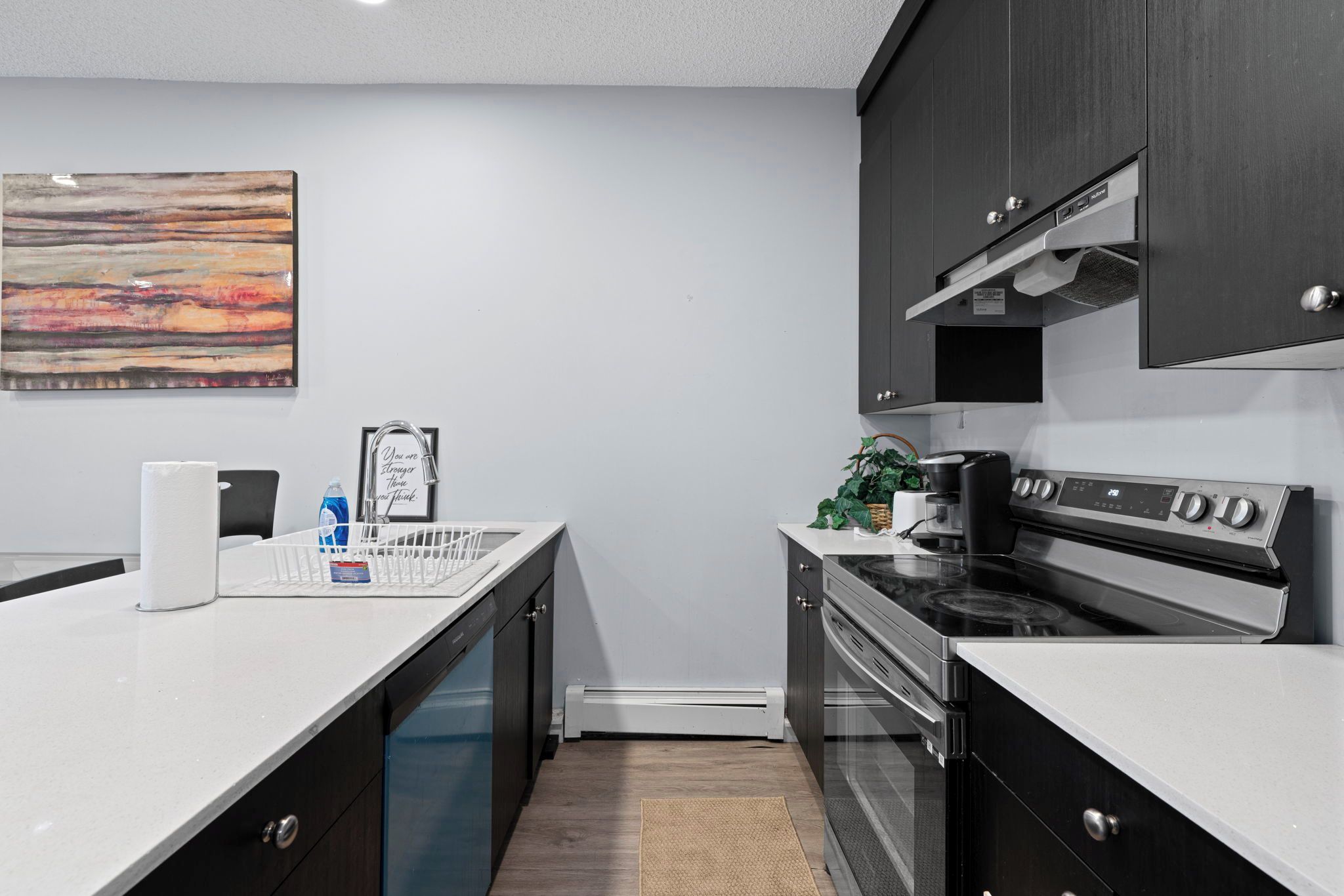 A modern kitchen with dark cabinetry, a white countertop, a stainless steel stove, and a dishwasher.