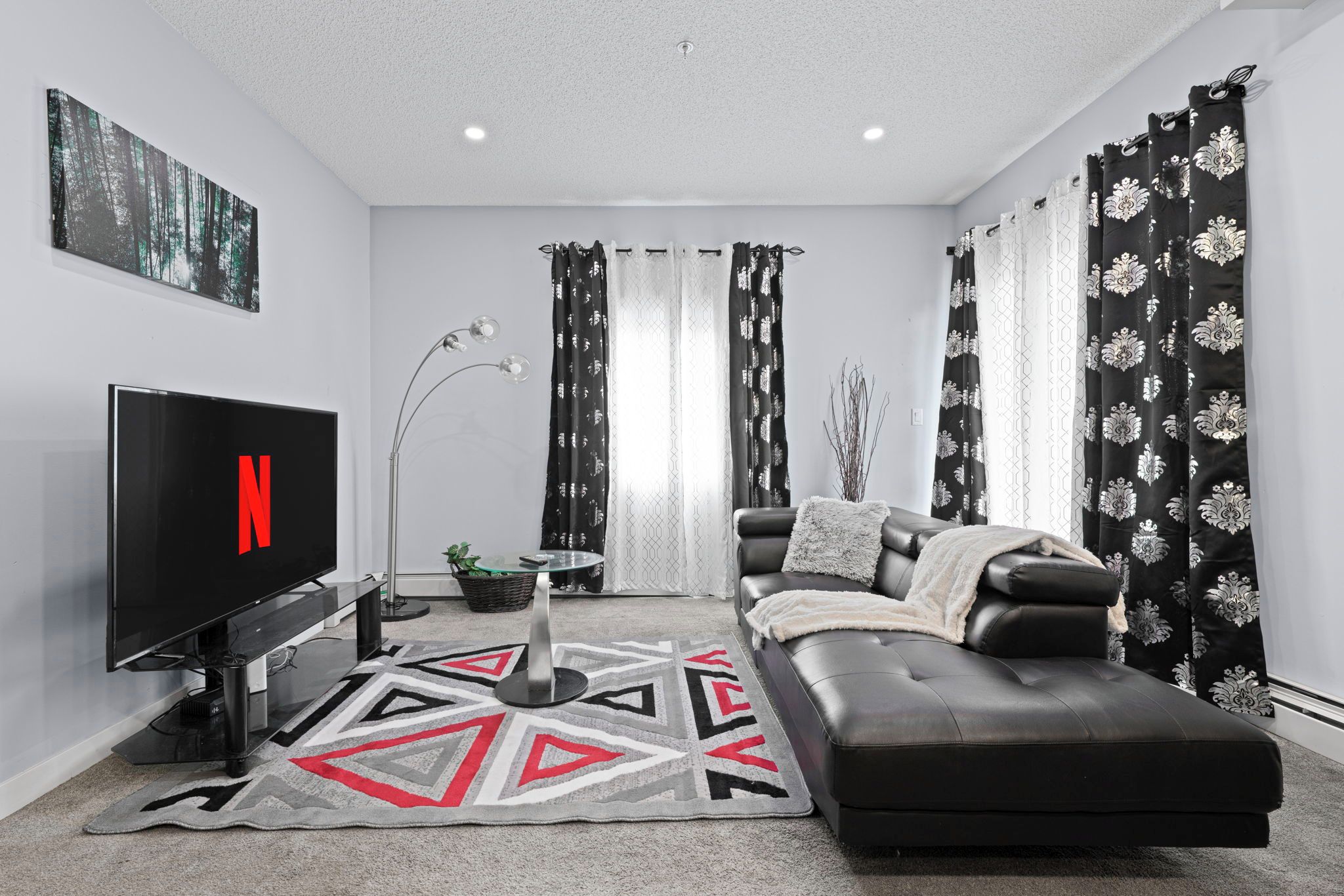 Un salon moderne avec un téléviseur à écran plat, un canapé, une table basse et un tapis décoratif.