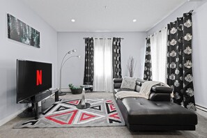 A modern living room with a flat-screen TV, a sofa, a coffee table, and a decorative rug.