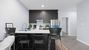 A modern kitchen with a central island, bar stools, and a dining table.