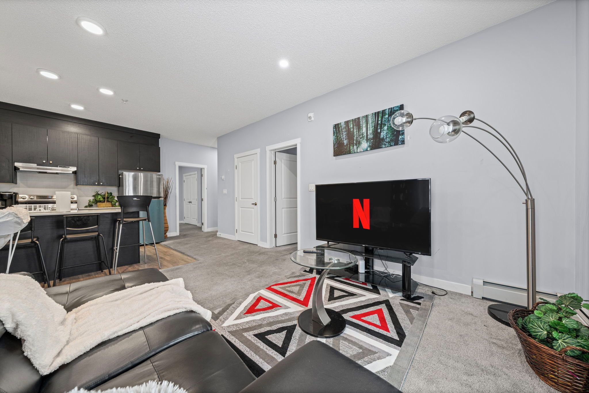 A modern living room with a flat-screen TV, a sofa, a coffee table, and a kitchen in the background.