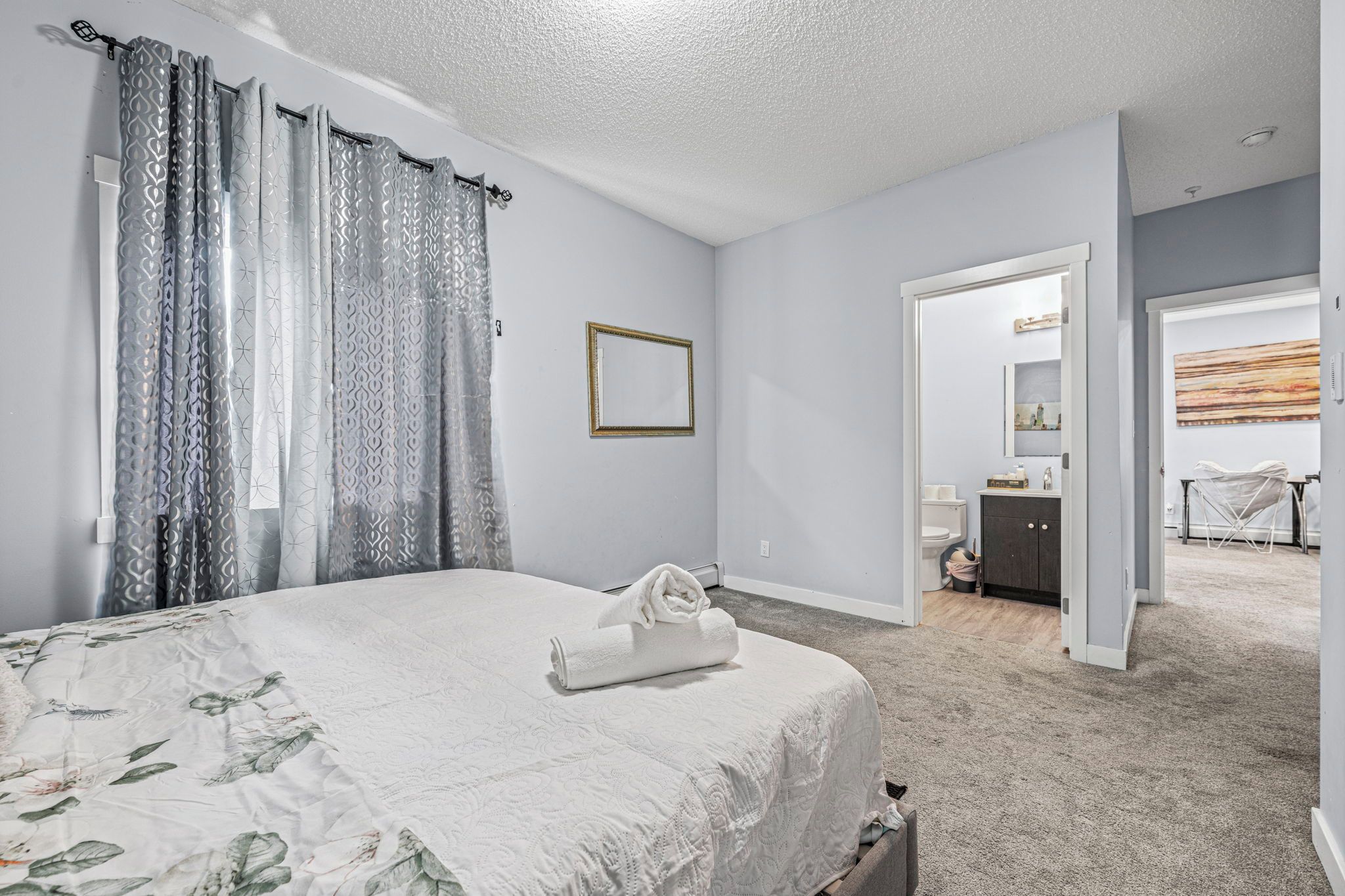 A bedroom with a bed, a bathroom visible through an open door, and a shower area.