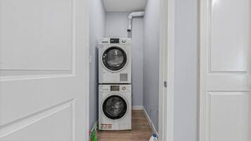 A laundry room with two stacked washing machines and a water bottle on the floor.