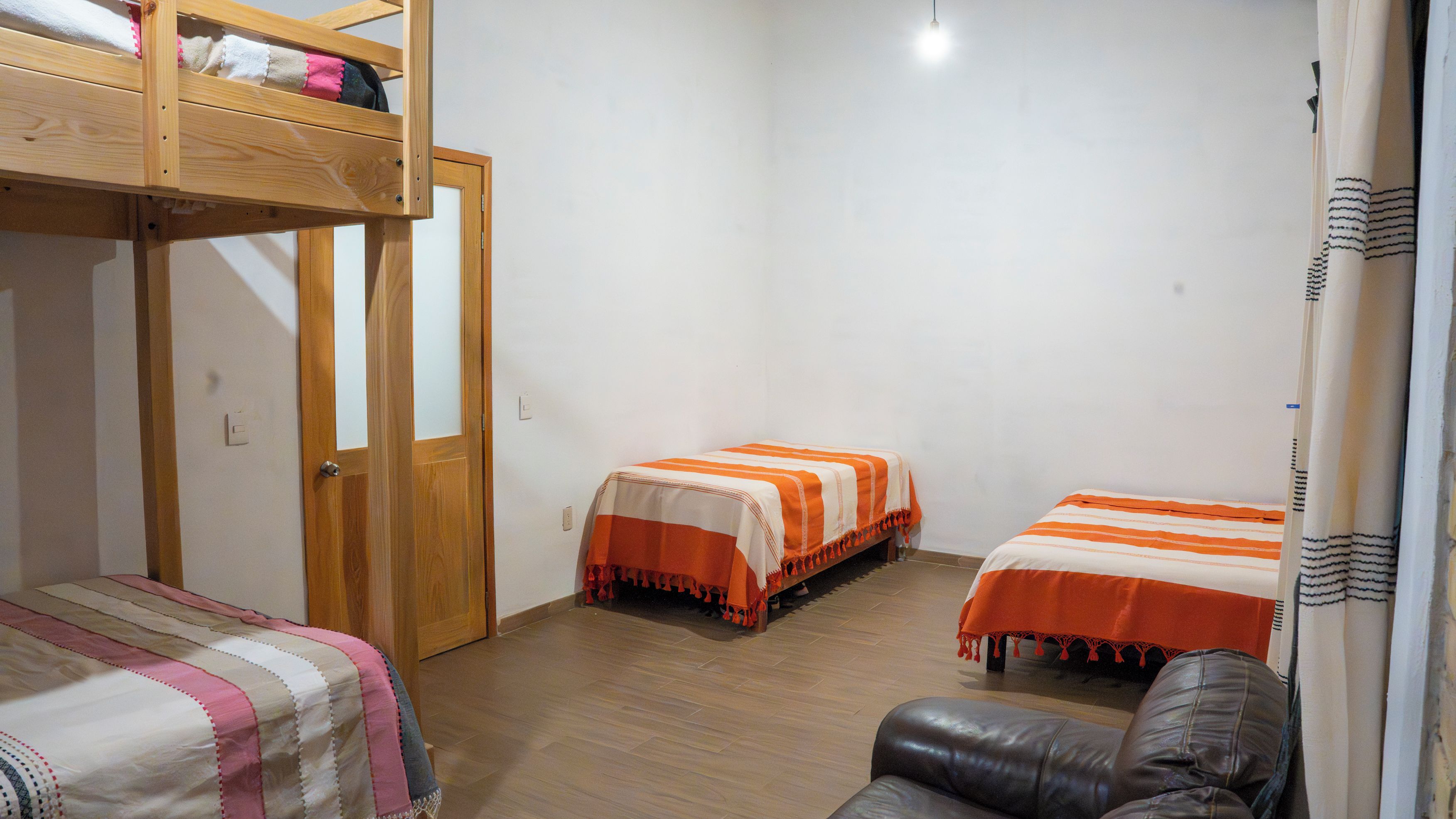 Une chambre avec des lits superposés, deux lits simples, un fauteuil en cuir et une porte en bois.