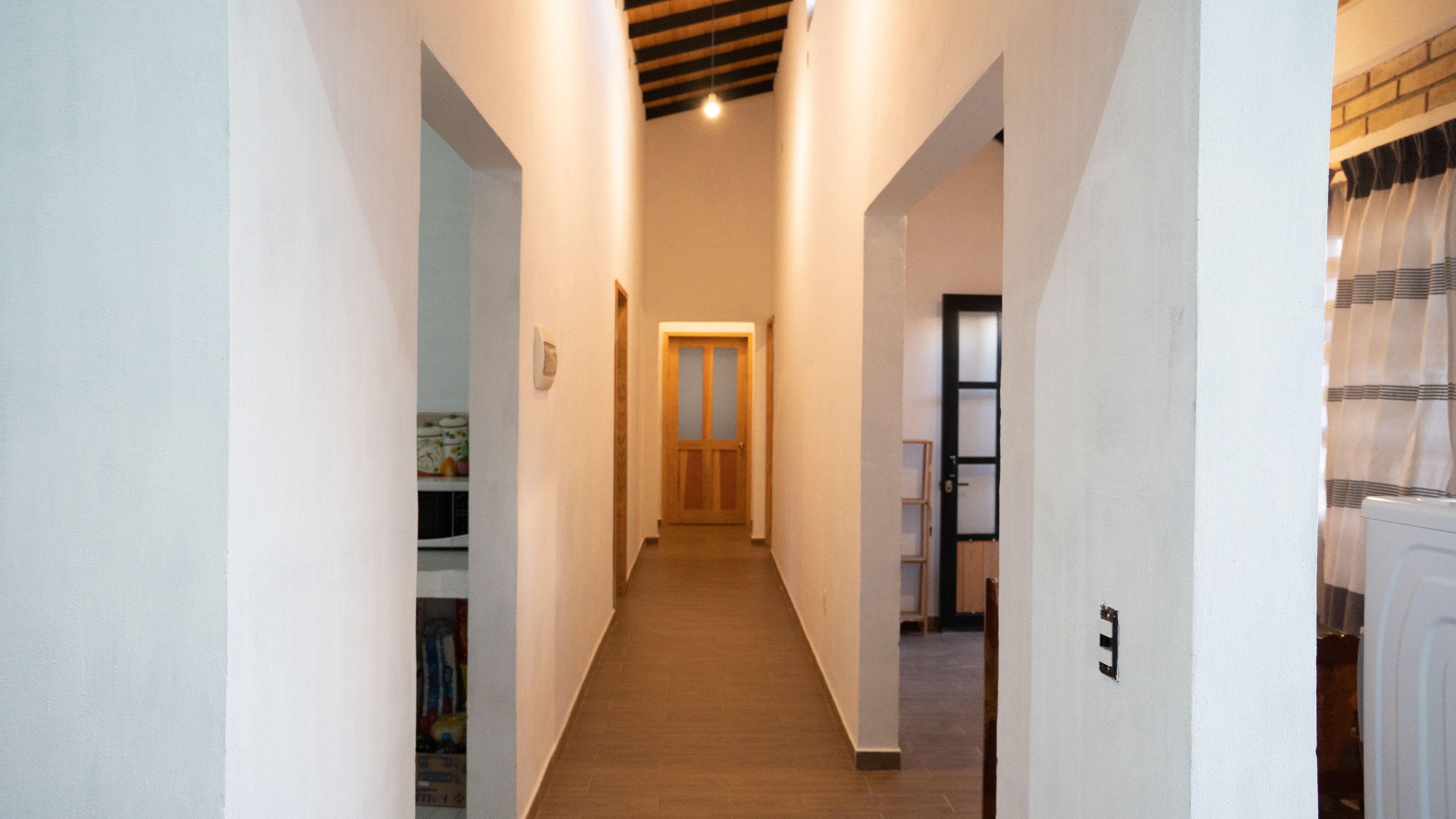 Un pasillo estrecho con una puerta de madera al final, que conduce a una habitación con suelo de baldosas.