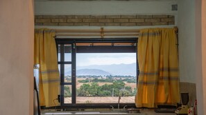 A window with yellow curtains, a view of a landscape with mountains, and a brick wall above.