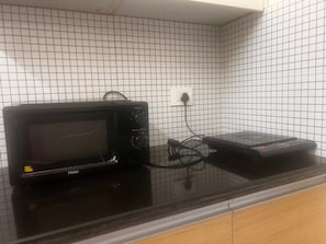 A kitchen with a black microwave on a black countertop, connected to a power outlet on the wall. - Private Apartment With Metro View on Highway (Mumbai)