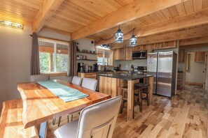 Un interno in legno con un tavolo da pranzo, sedie, angolo cottura con elettrodomestici e una finestra che lascia entrare luce naturale.