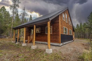 Una baita di legno con veranda, diverse finestre e un vialetto sterrato.