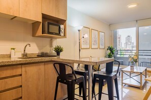 A modern kitchen with a microwave, bar stools, and a view of the city through large windows. - Santa Rosa Apartments by Andes with Parking (Santiago)