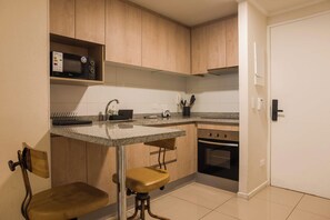 A kitchen with wooden cabinets, a microwave, a sink, a stove, and two stools. - Santa Rosa Apartments by Andes with Parking (Santiago)