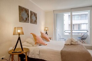 A hotel room with a bed, two bedside lamps, a blanket, a chair, and a window with a view of buildings. - Santa Rosa Apartments by Andes with Parking (Santiago)