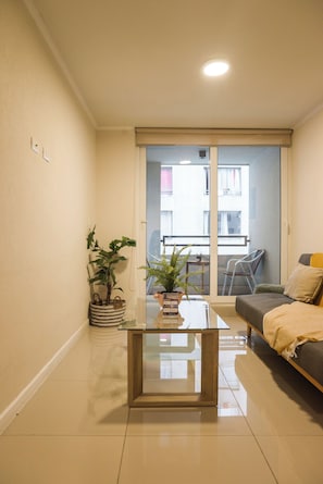 A modern living room with a glass coffee table, two potted plants, a sofa, and a sliding glass door leading to a balcony. - Santa Rosa Apartments by Andes with Parking (Santiago)