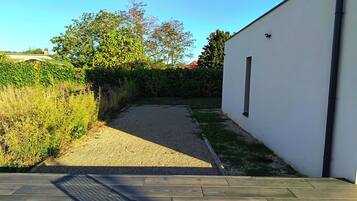 Een geplaveid pad leidt naar een wit gebouw met een raam, omringd door groen en een heldere lucht.