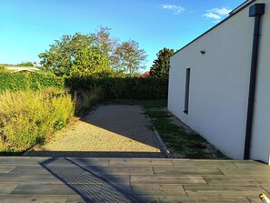 Un vialetto lastricato conduce a un edificio bianco con una finestra, immerso nel verde e sotto un cielo sereno.