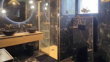 Een badkamer met een zwart marmeren wastafel, een spiegel en een douchecabine.