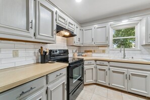 A kitchen with white cabinetry, a black stove, and a window with a view of trees. - Charming 3-bedroom house in adorable Edmond with quick access to I-35 or US-77 (Edmond)