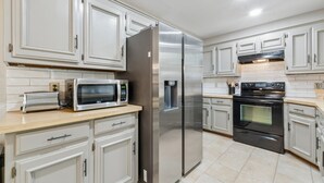 Une cuisine moderne avec des meubles blancs, des appareils en acier inoxydable, notamment un réfrigérateur, un four à micro-ondes et un four, et un dosseret carrelé.