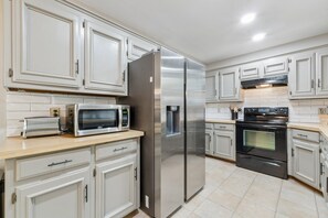 Una cocina moderna con armarios blancos, electrodomésticos de acero inoxidable, incluyendo un refrigerador, microondas y horno, además de un salpicadero de azulejos.