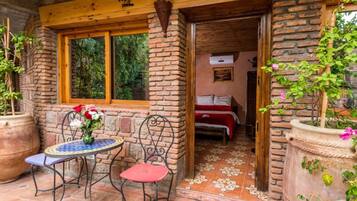 Quarto rústico com lareira de tijolos, cama com roupa de cama vermelha e janela com vista para o verde.