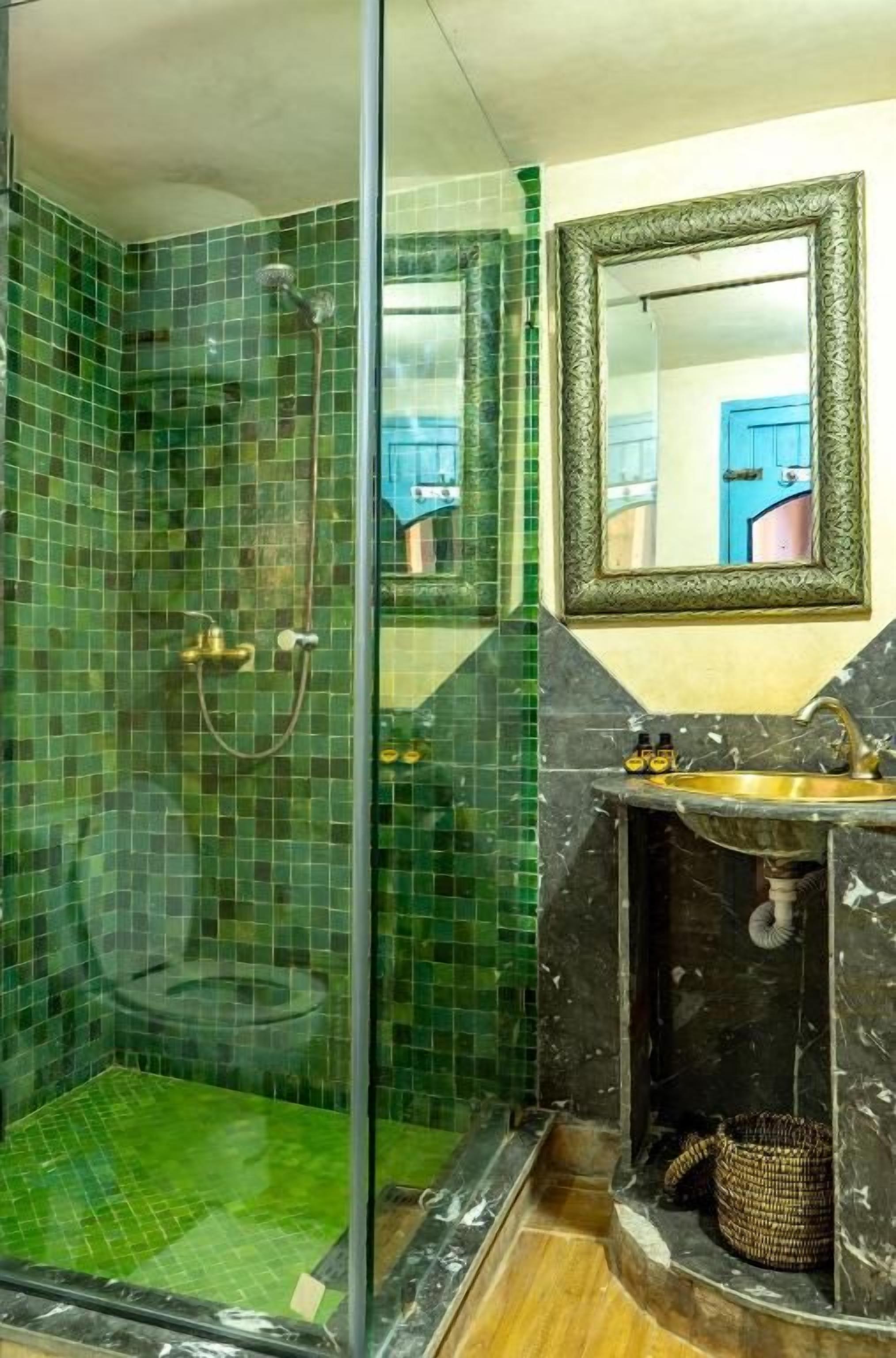 A bathroom with a glass shower enclosure, a sink with a marble countertop, and a mirror with a decorative frame.