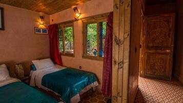 A room with two beds, wooden ceiling, a door with a panel, and a window with curtains.