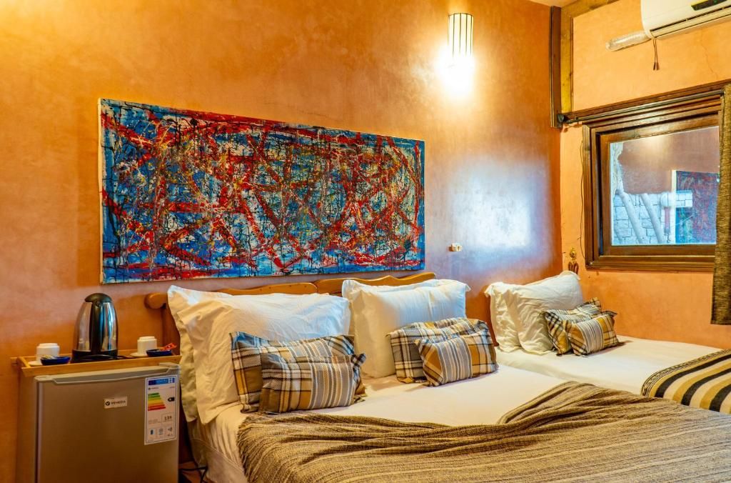 A hotel room with a bed, pillows, a coffee machine, and a large abstract painting on the wall.