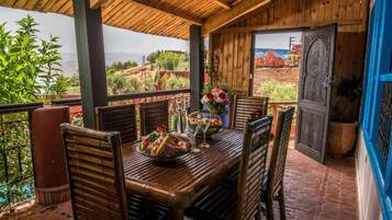 Un área de comedor al aire libre con una mesa y sillas de madera, vistas al paisaje y una puerta con un panel decorativo.
