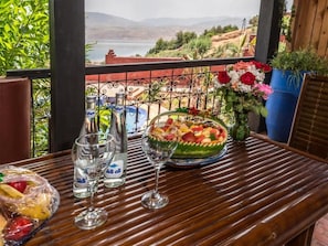 A table with a fruit bowl, water bottles, and a watermelon carved into a bowl on a balcony with a view of a lake and mountains. - Hotel Bin El Ouidane (Bine el Ouidane)