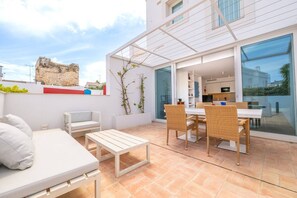 A modern outdoor living area with a sofa, dining table, and chairs, connected to a glass door leading to a kitchen. - Les Terrasses B / Private Rooftop Pool in Tavira (Faro)