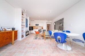A modern kitchen with white cabinets, a dining area with blue chairs, and a living room with a sofa. - Les Terrasses B / Private Rooftop Pool in Tavira (Faro)