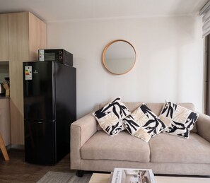 A modern living room with a black refrigerator, a beige sofa with patterned cushions, a round mirror on the wall, and a magazine on the coffee table. - Edificio Link Ecuador by Domus Travels (Estación Central)