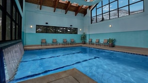 Een binnenzwembad met helderblauw water, omringd door ligbedden en potplanten.
