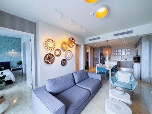 A modern living room with a grey sofa, a dining area with blue chairs, and a kitchen with grey cabinets. - Coastal Paradise 2BR Marina View (Rio Hato)