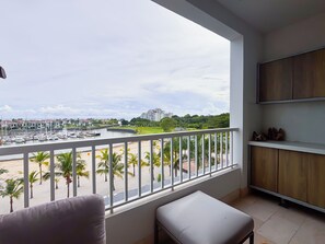 A balcony with a view of a marina and buildings, a white cushioned bench, and wooden cabinets. - Coastal Paradise 2BR Marina View (Rio Hato)