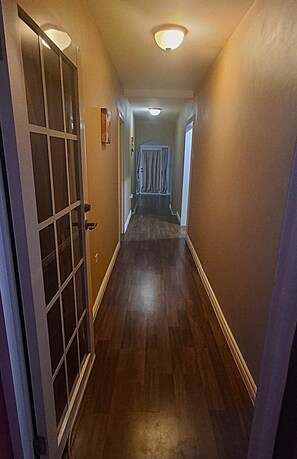 A narrow hallway with wooden flooring, a door with glass panels, and a ceiling light fixture. - Akim's Apartments (Scarborough)