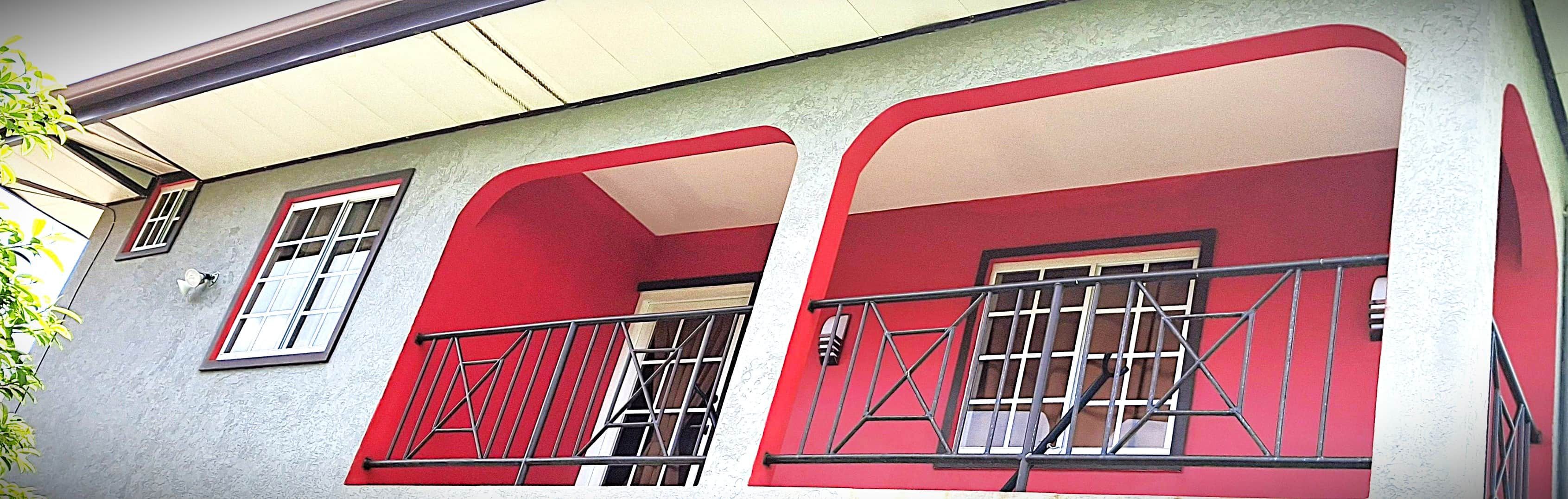 A building with a red facade, multiple windows with metal bars, and a visible door.