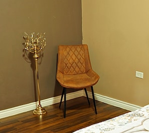 A corner room with a wooden floor, a brown wall, and a single chair with a diamond pattern backrest.