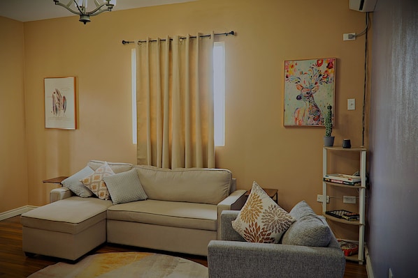 A living room with a beige sofa, a grey armchair, a patterned rug, and a painting on the wall.