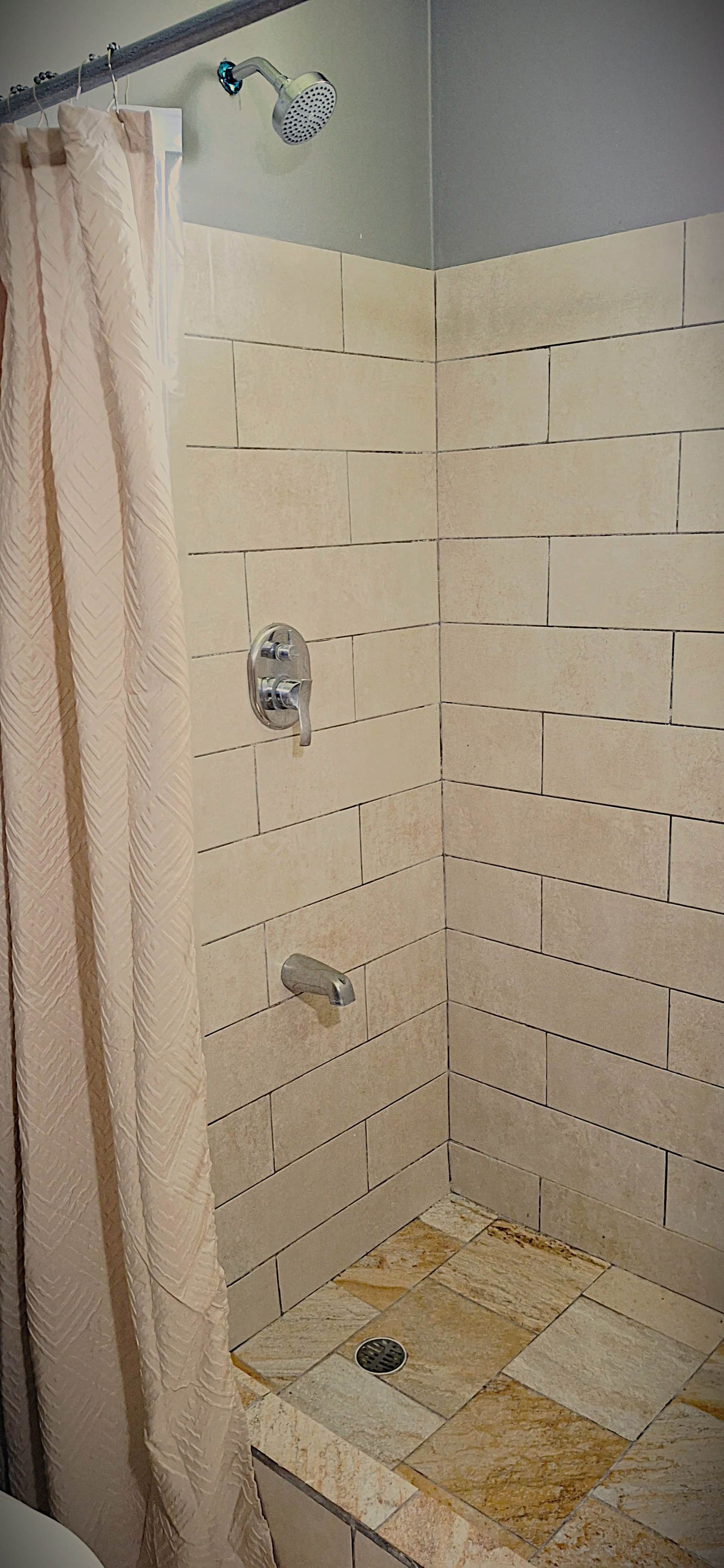 A shower with a tiled wall, a showerhead, and a drain.